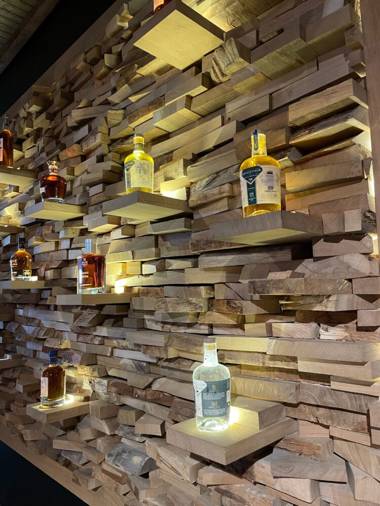 Oak stave wall displaying Cognac bottles, symbolizing the aging process and the alchemy between wood and eau-de-vie